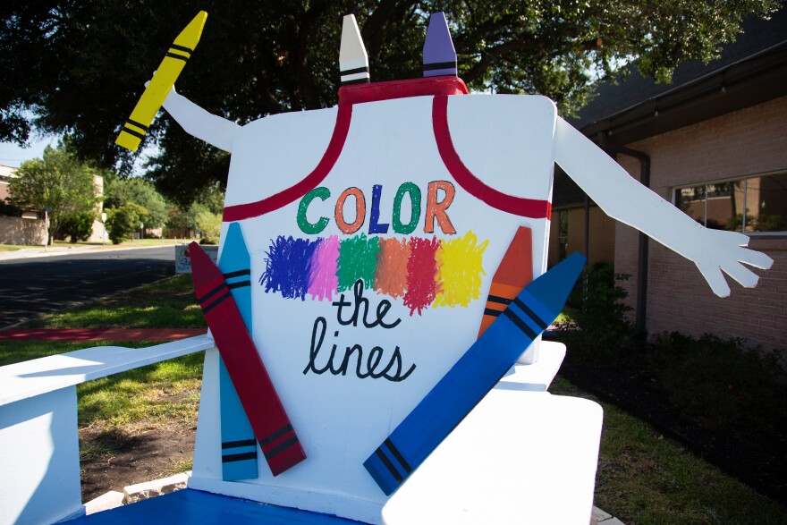 A giant Adirondack chair sits outside with crayon drawings and Color Outside the Lines written on it. 