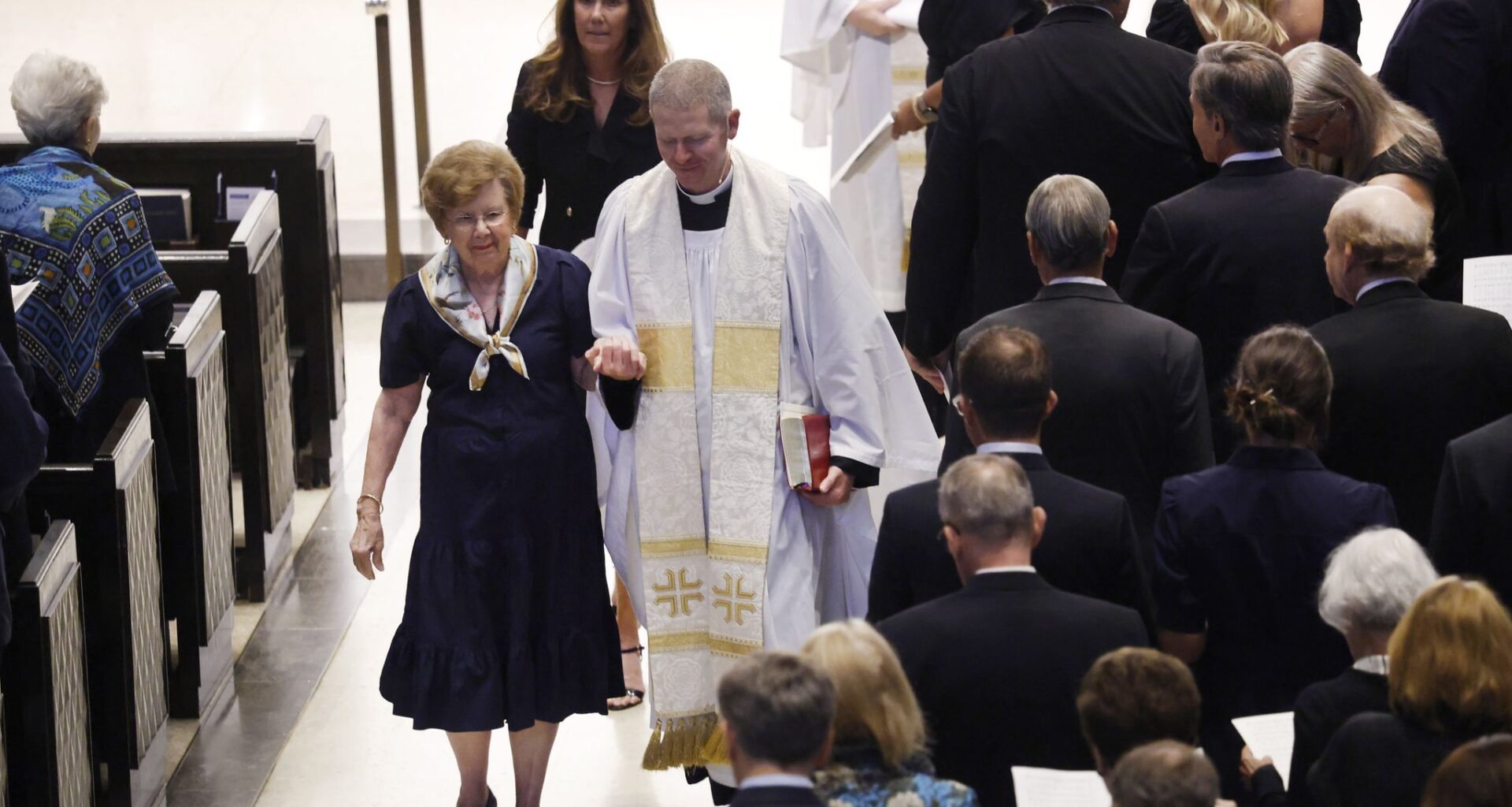 The Reverend Dr. Christopher D. Girata escorts Pam Luce, widow of the late Tom W. Luce III, from Saint Michael and All Angels Episcopal Church sanctuary following a service for her husband in Dallas, August 15, 2026. The influential Dallas attorney, public policy reformer, and civic leader passed away at the age of 86.
