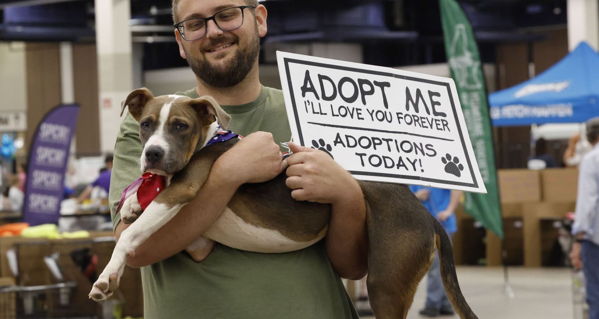 Mark Johnson of Arlington Animal Services holds Dougie, a seven-month-old dog, and a sign during the MEGA Adoption Event, Sunday, Aug. 16, 2026, at Amon G. Carter Jr. Exhibits Hall in Fort Worth. The event featured dogs, cats, and other small furry pets, sponsored by the Humane Society of North Texas.