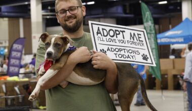 Mark Johnson of Arlington Animal Services holds Dougie, a seven-month-old dog, and a sign during the MEGA Adoption Event, Sunday, Aug. 16, 2026, at Amon G. Carter Jr. Exhibits Hall in Fort Worth. The event featured dogs, cats, and other small furry pets, sponsored by the Humane Society of North Texas.