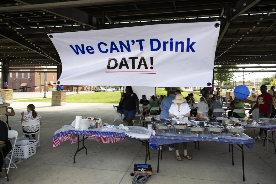 A person stands at a table with food under a large white banner that reads "We CAN'T Drink DATA!"