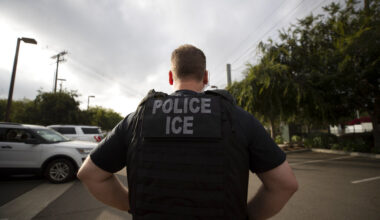 In this July 8, 2019, file photo, a U.S. Immigration and Customs Enforcement (ICE) officer looks on during an operation in Escondido, Calif. Advocacy groups and unions are pressuring Marriott, MGM and others not to house migrants who have been arrested by U.S. Immigration and Customs Enforcement agents. But the U.S. government says it sometimes needs bed space, and if hotels don’t help it might have to split up families.