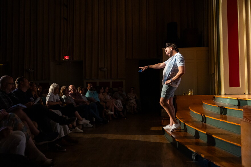 A person standing on the steps of a theater stage points out at audience members.