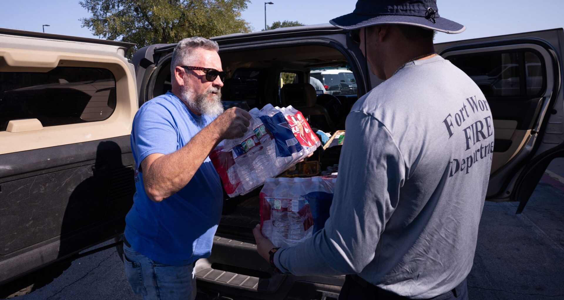 Marty Goin hands donated water to Fort Worth Firefighter/EMT Elfidio Quiñónez as the Fort Worth Police Department South Division hosts a supply drive in Fort Worth, Saturday, Aug. 29, 2026. The department collected donations to support the firefighters working to battle the Ross fire.