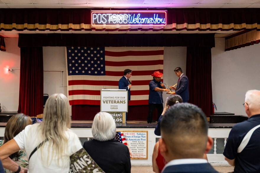 U.S. House Speaker Mike Johnson (R-Louisiana) and 35th Congressional District Republican nominee Carlos De La Cruz accept a gift from VFW Post Commander Ralph Alvarado during a visit in San Antonio on Wednesday, Aug. 26, 2026.