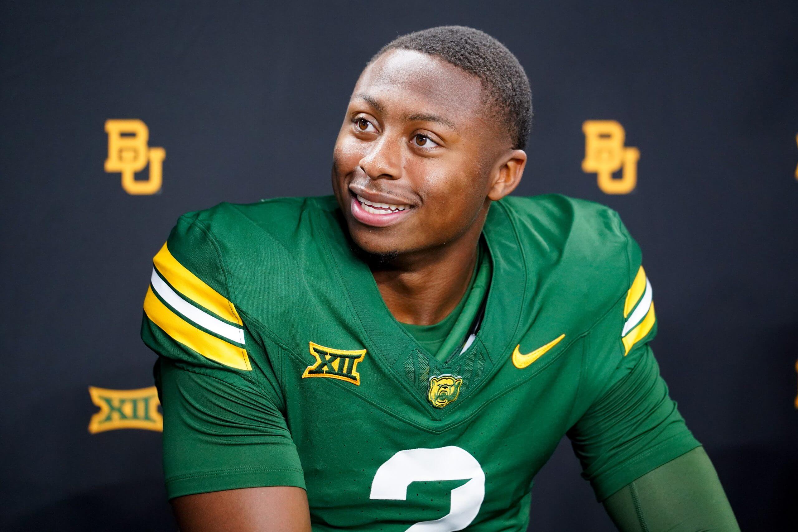 DJ Lagway, wearing a Baylor jersey with no helmet, smiles and looks to his left