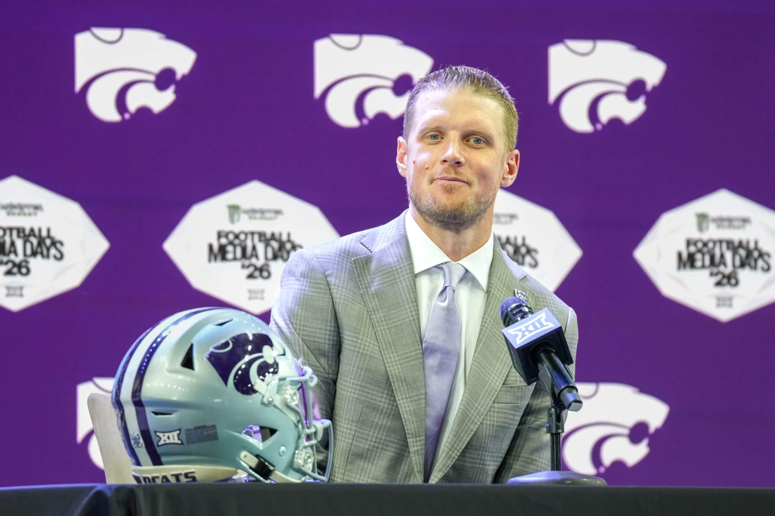Collin Klein sits behind a microphone and a Kansas State helmet