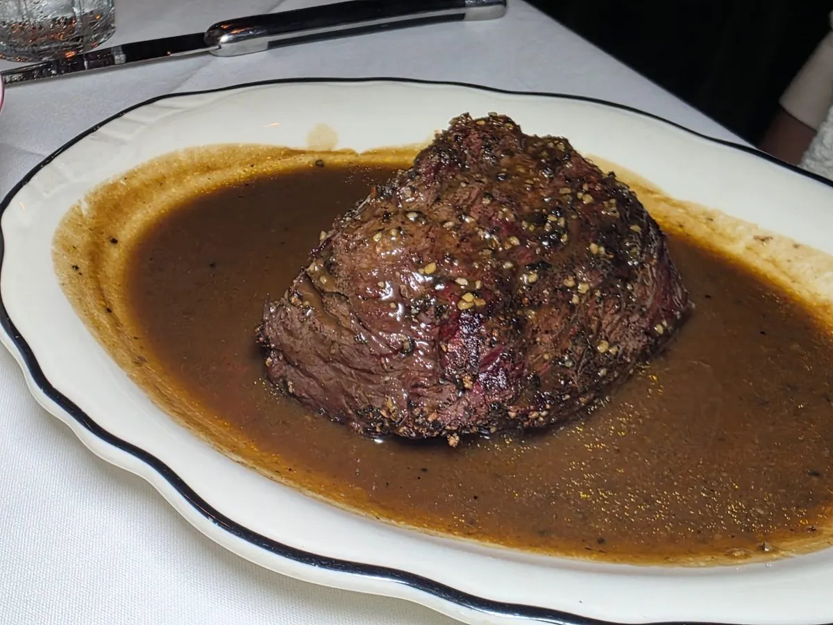 The petite filet mignon arrives on a plate, one of the restaurant's many beautiful Homer Laughlin China pieces, with pan sauce, adding another savory layer without overwhelming the meat. Photo by Mario-Sebastian Berry.
