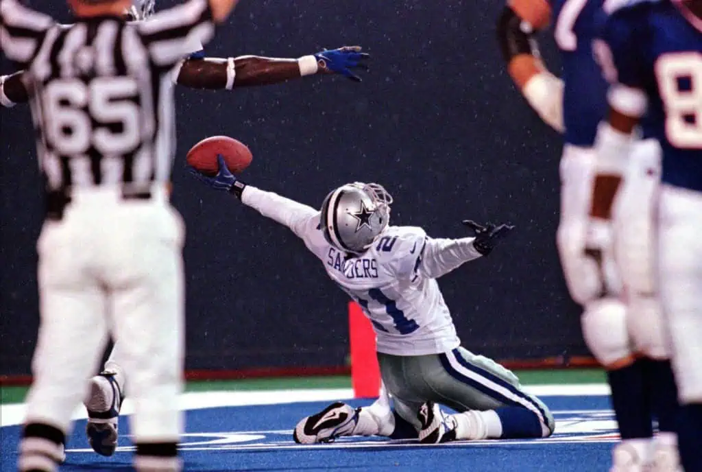 Could Dallas Pull Off A Deion Sanders-Level Move? Deion Sanders stretches the football out in one hand while celebrating on the field for the Dallas Cowboys.