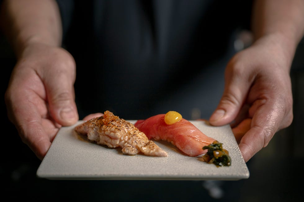 Two pieces of sushi presented on a plate, one with toppings and the other garnished with an egg yolk and vegetables.