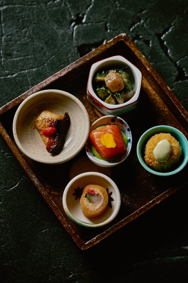A tray containing various colorful Japanese small dishes with fish, vegetables, and garnishes.
