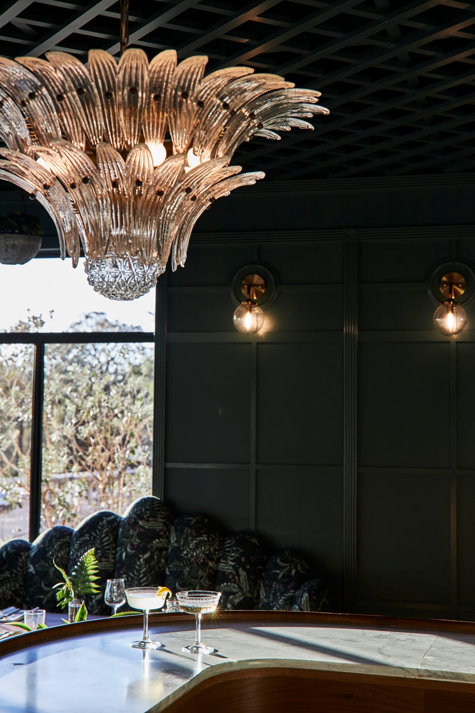 Chandelier above a bar with two cocktails and modern decor in a stylish interior setting.