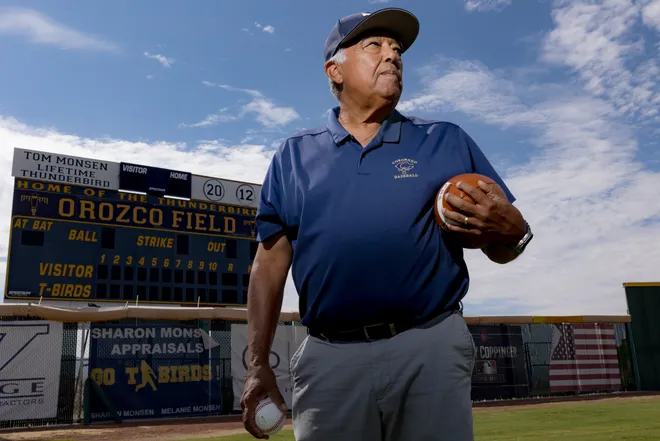Juan “Choppy” Orozco, a longtime Coronado High School baseball coach and assistant football coach who is retiring after 47 years, stands next to a scoreboard with his name Wednesday, Aug. 12, 2026, at Coronado High School in West El Paso, Texas.