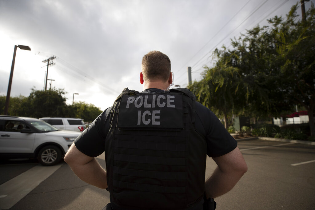 In this July 8, 2019, file photo, a U.S. Immigration and Customs Enforcement (ICE) officer looks on during an operation in Escondido, Calif. Advocacy groups and unions are pressuring Marriott, MGM and others not to house migrants who have been arrested by U.S. Immigration and Customs Enforcement agents. But the U.S. government says it sometimes needs bed space, and if hotels don't help it might have to split up families.