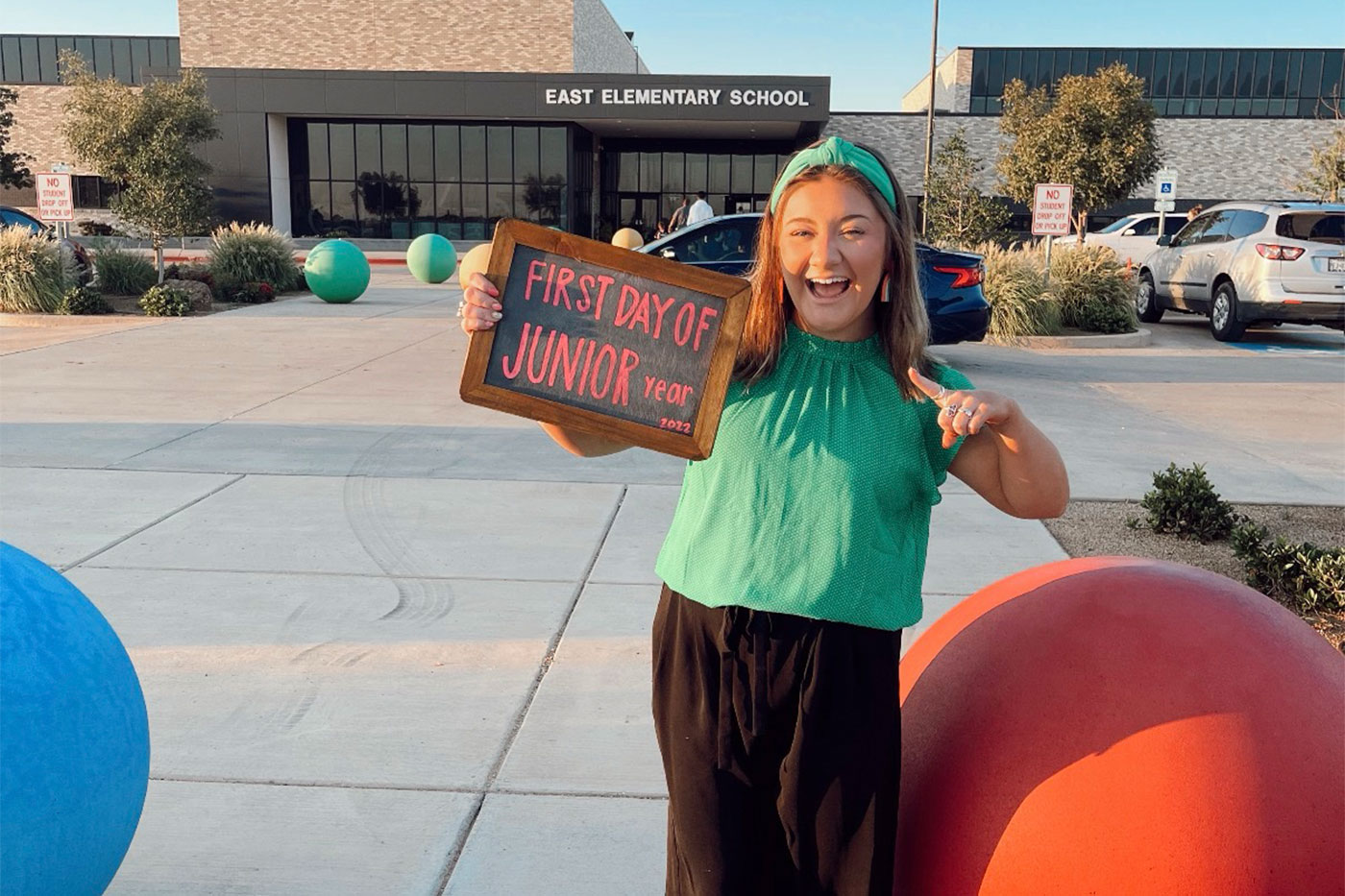 A smiling student, Braeley Krautsch, stands outside East Elementary School holding a sign that reads “First Day of Junior Year 2022.”