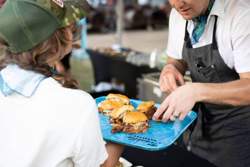 Image shows a chef handing a plate of barbecue to an attendant at the Southern Smoke Festival. 