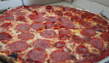 Ghost Pizza with pepporoni and hot cups laid across the top. Red sauce peeps above blackened thick crust.