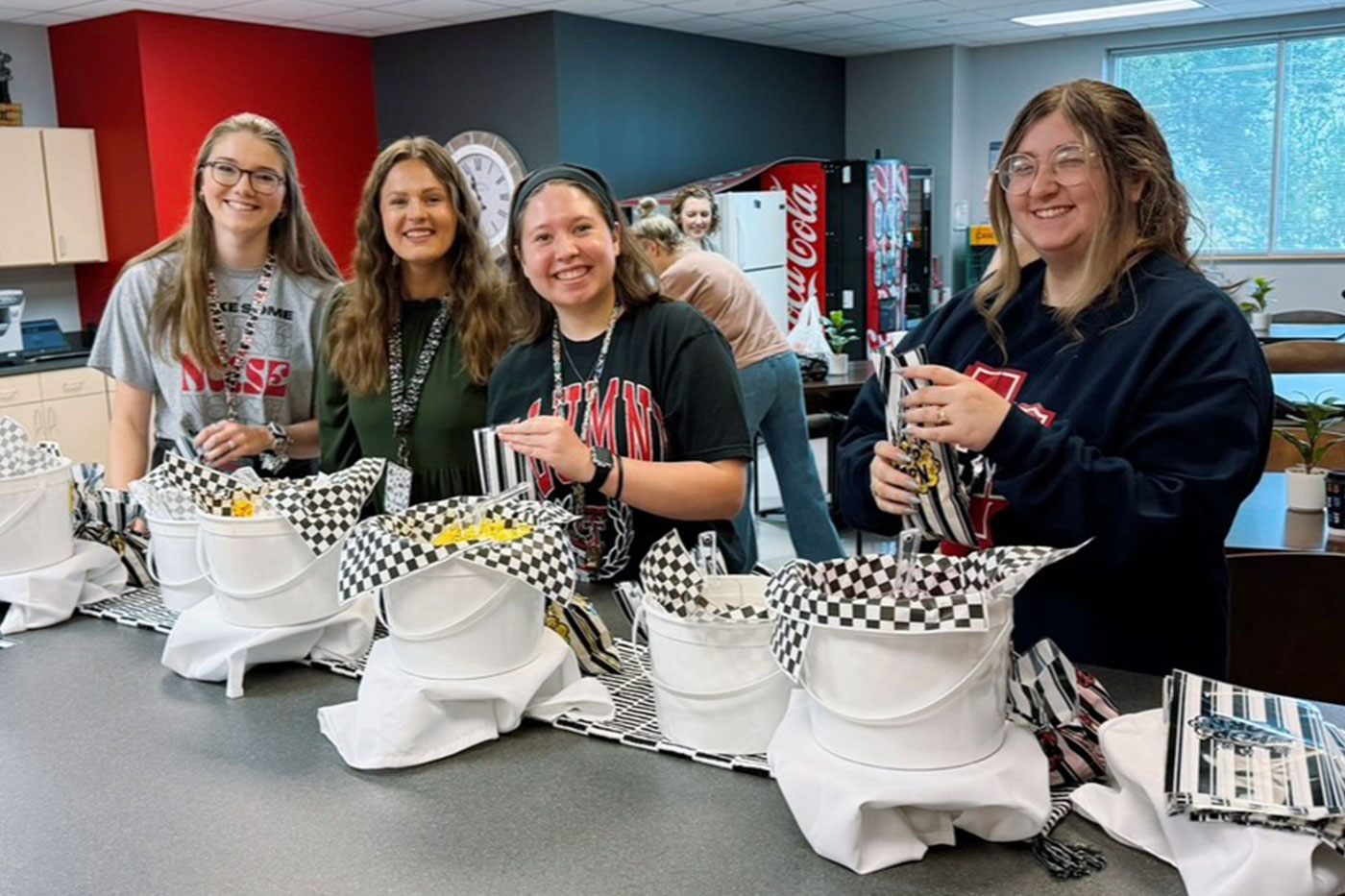 Four students stand behind a counter assembling gift baskets or event favors.