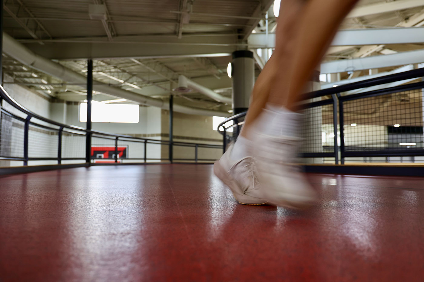 A blurred shot of a foot in a tennis shoe, running on an indoor track.