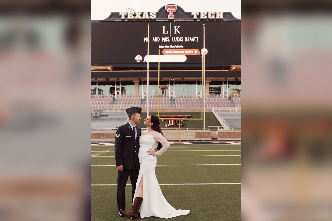 A newlywed couple poses on the Texas Tech football field in front of the stadium scoreboard.