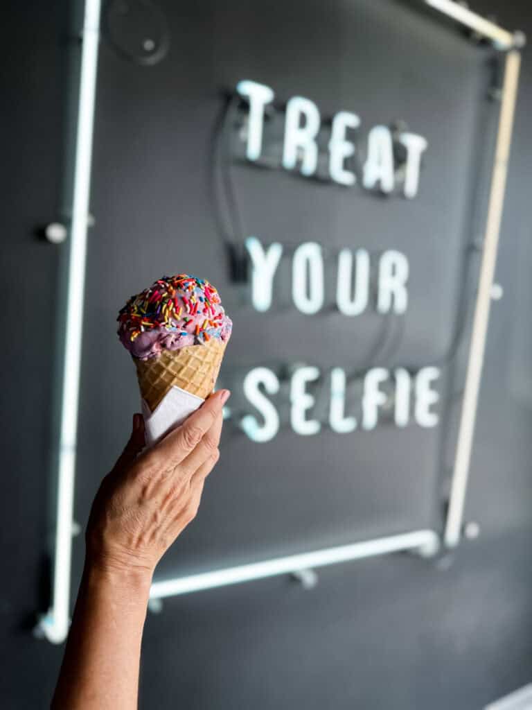 Hand holding an ice cream cone with sprinkles in front of a sign.