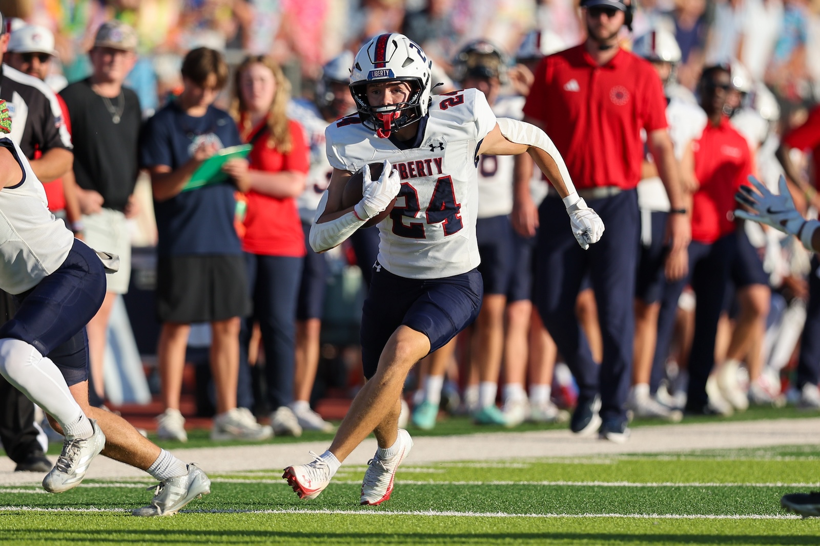 Football player wearing a white Liberty jersey #24 runs with the ball during a game, crowded sideline in the background.