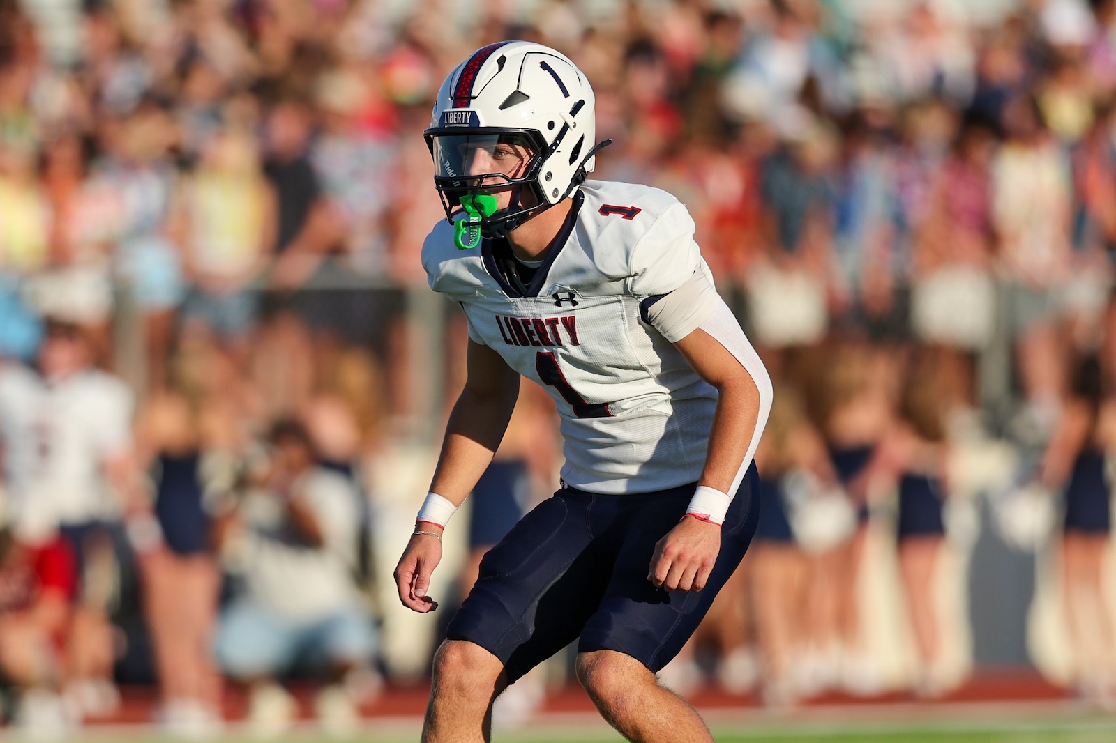 American football player in a white Liberty jersey numbered 1 on a sunny field with a cheering crowd in the background.