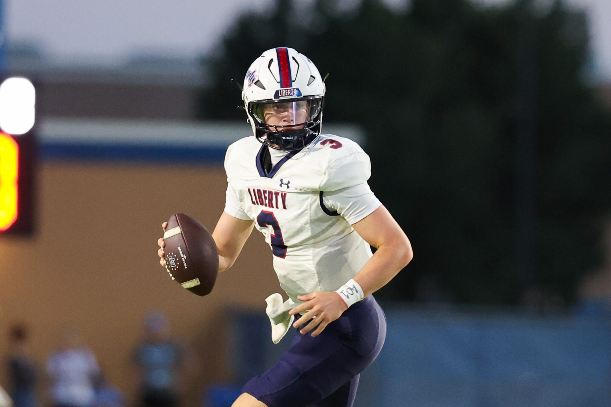 Football player in a white Liberty jersey runs with the ball during a game, wearing a white helmet with a red stripe.