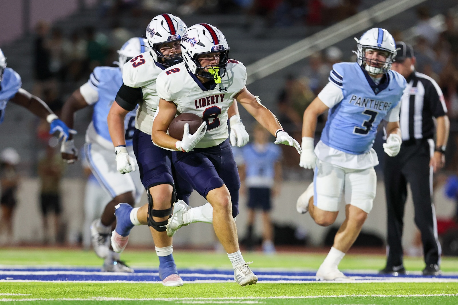 Liberty player (#3) carries the football downfield as defenders from the Panthers pursue during a nighttime football game.