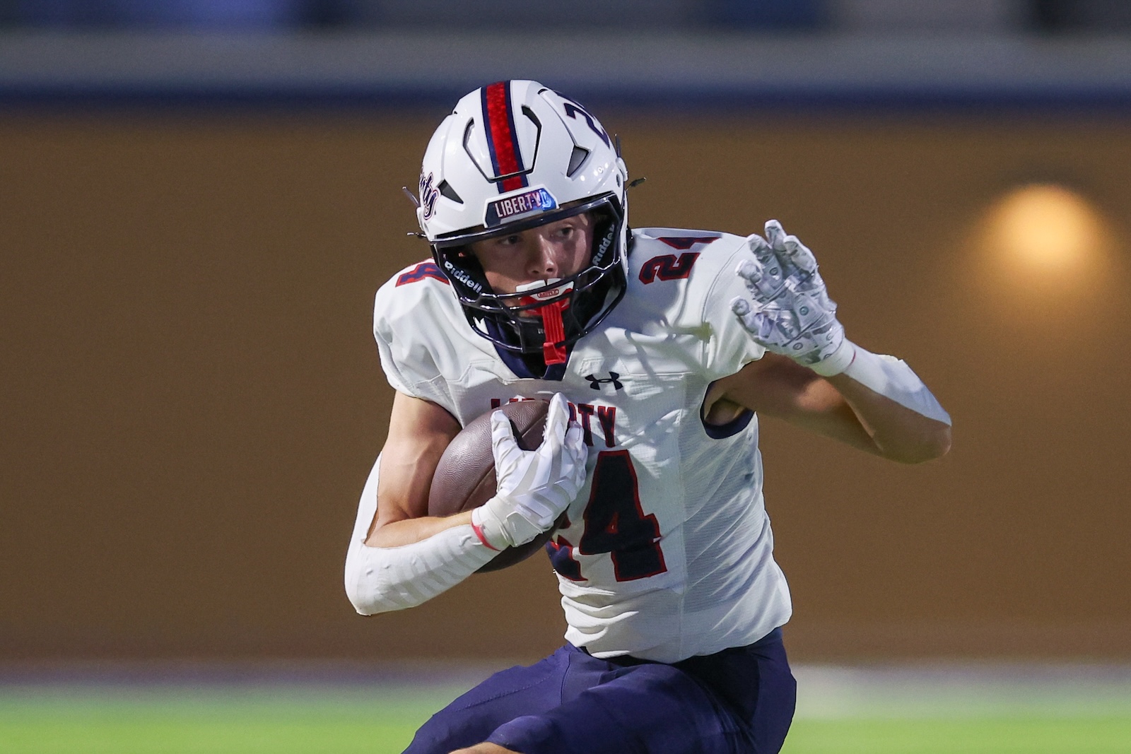 Football player in white jersey holding a ball and running forward, number 4 visible, purple pants, motion shot on field