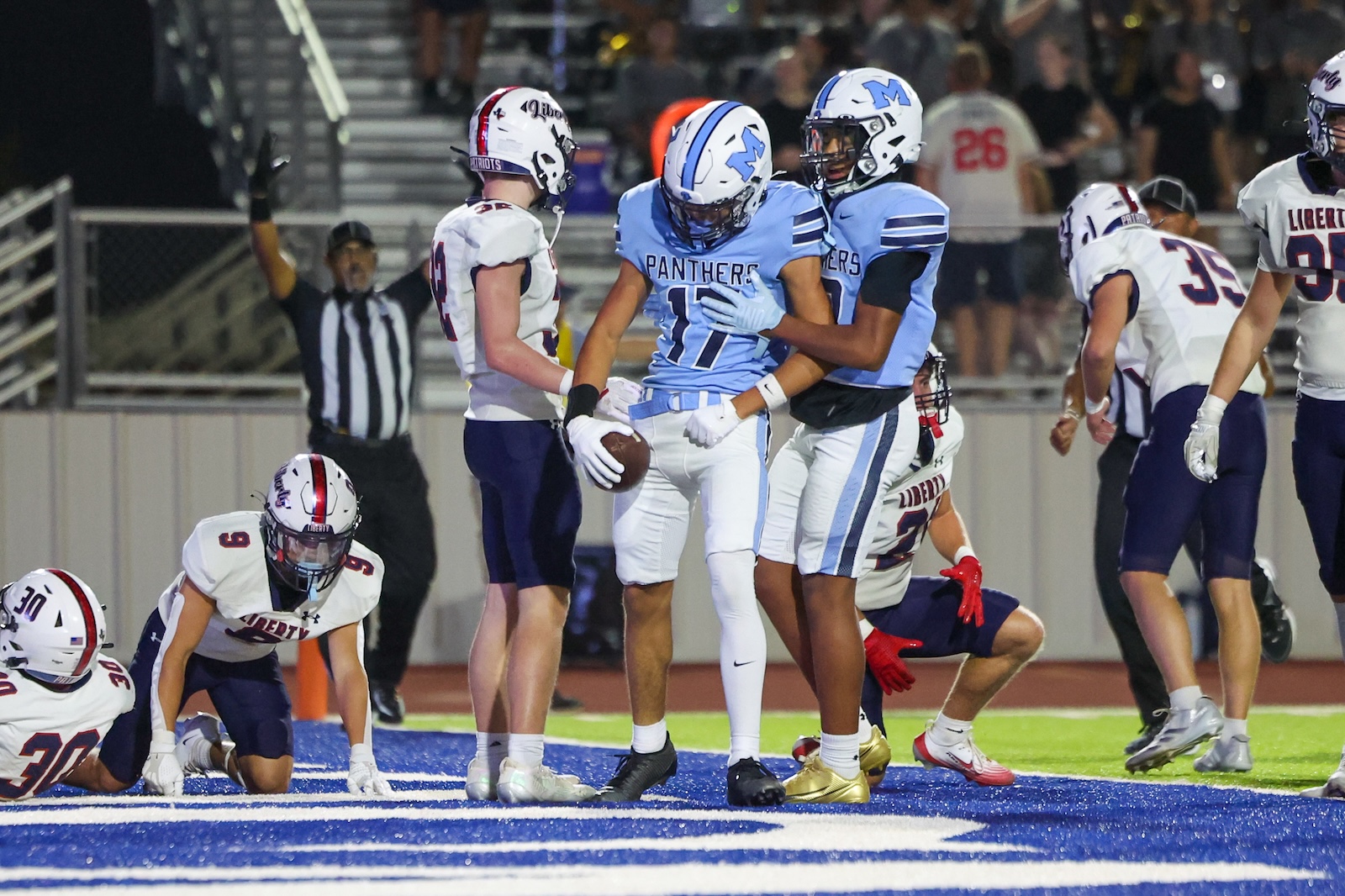 Panthers player in blue jersey (#11) holds a football while a teammate in blue supports him in the end zone, surrounded by opponents in white uniforms.