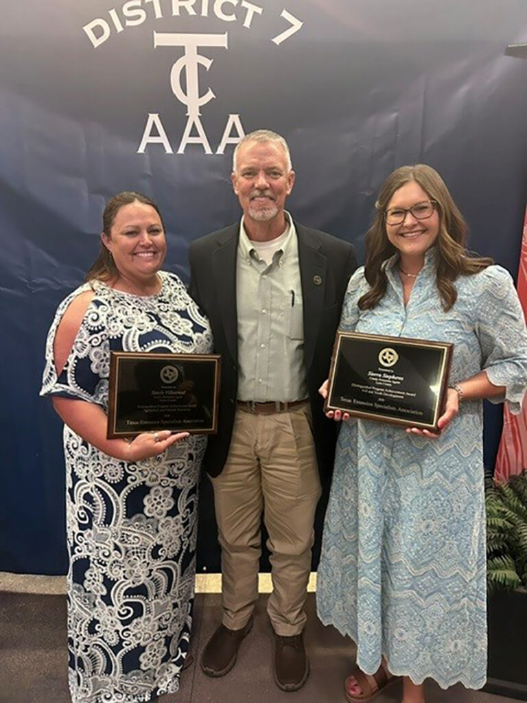 a man stands between two women who are each holding a plaque
