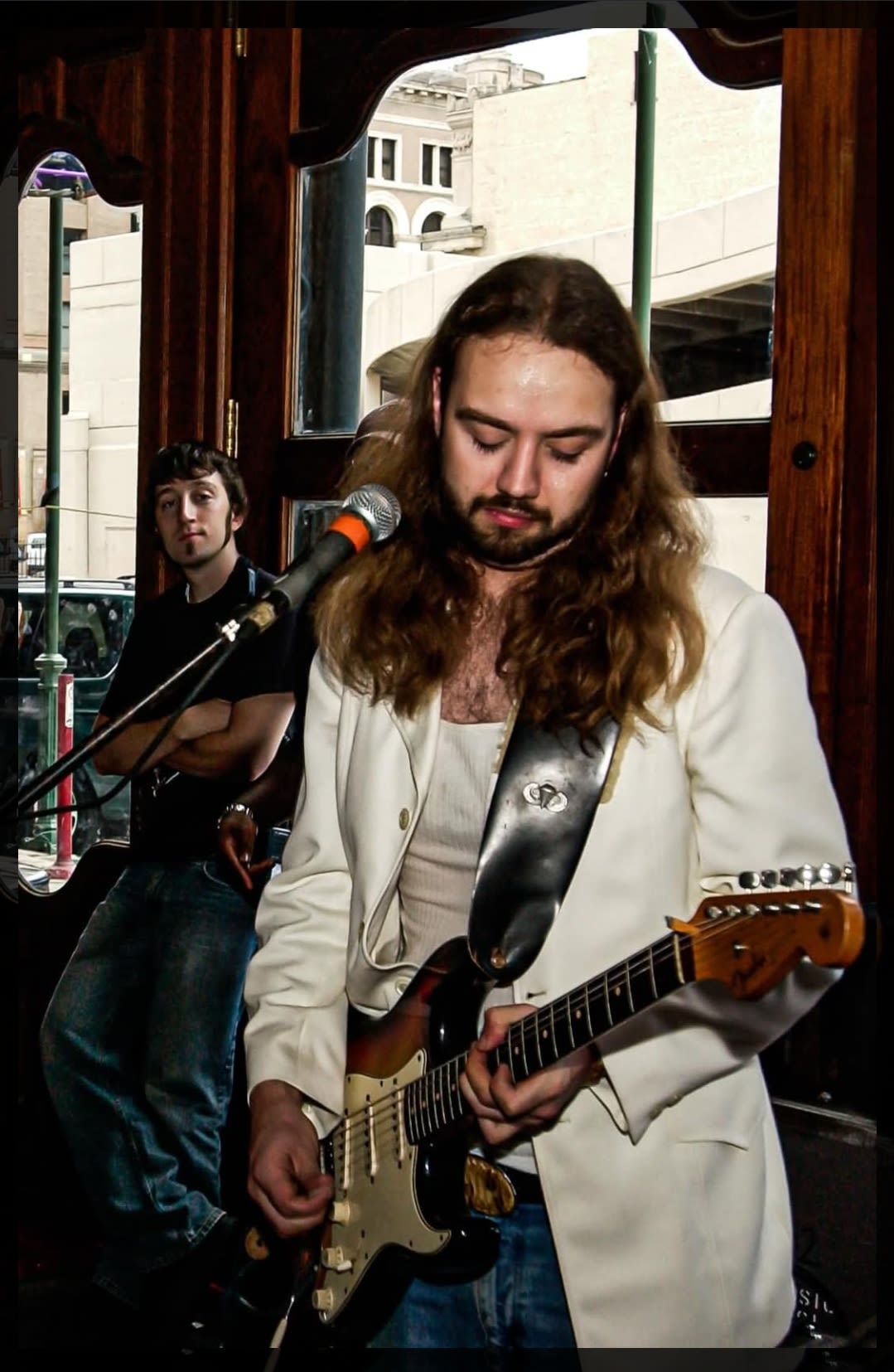 A bearded, long-haired man playing guitar at a show.