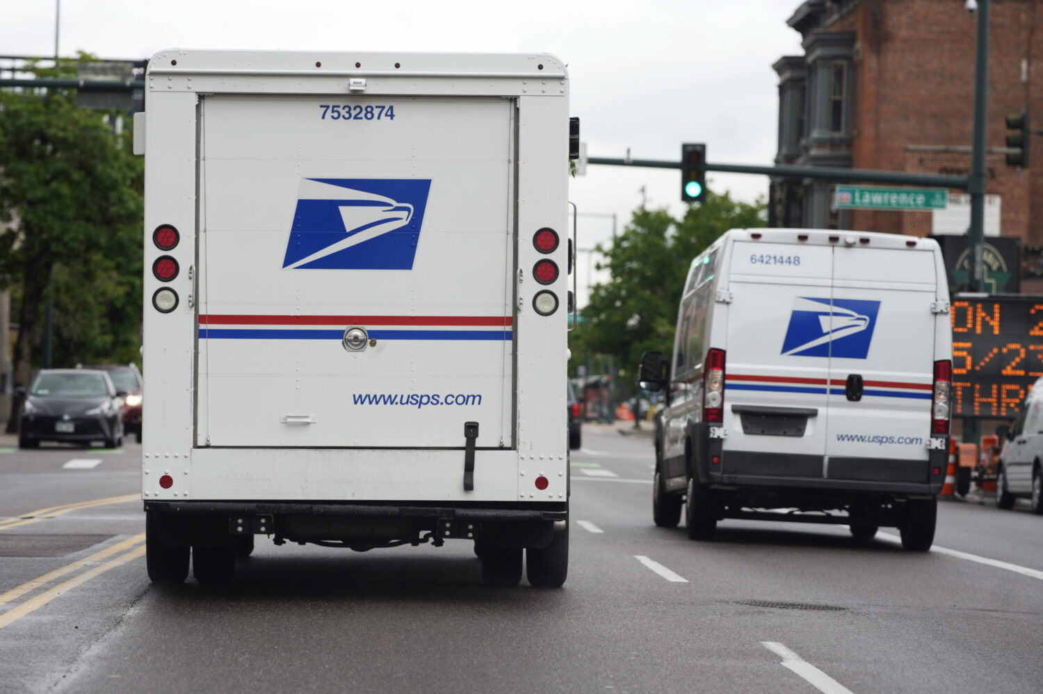 FILE - A USPS logo adorns the back doors of United States Postal Service delivery vehicles as they proceed westbound along 20th Street from Stout Street and the main post office in downtown Denver, Wednesday, June 1, 2022. USPS plans to substantially increase the number of electric-powered vehicles it