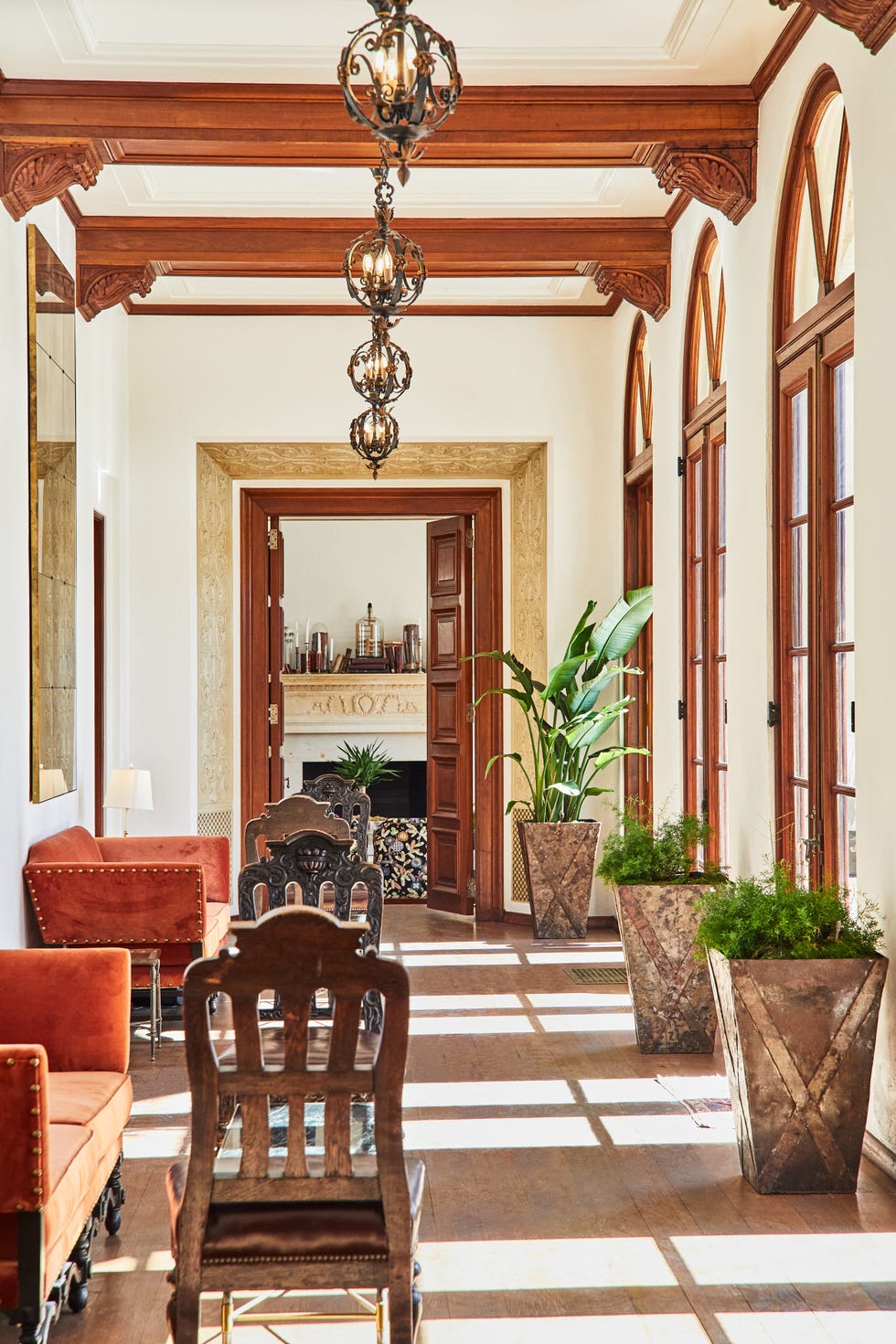 Bright hallway featuring ornate wooden beams, decorative lamps, plants, and cozy seating arrangements.