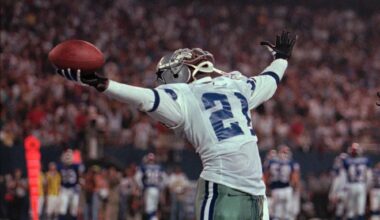 Deion Sanders celebrates while holding the football high in one hand during a Dallas Cowboys game.