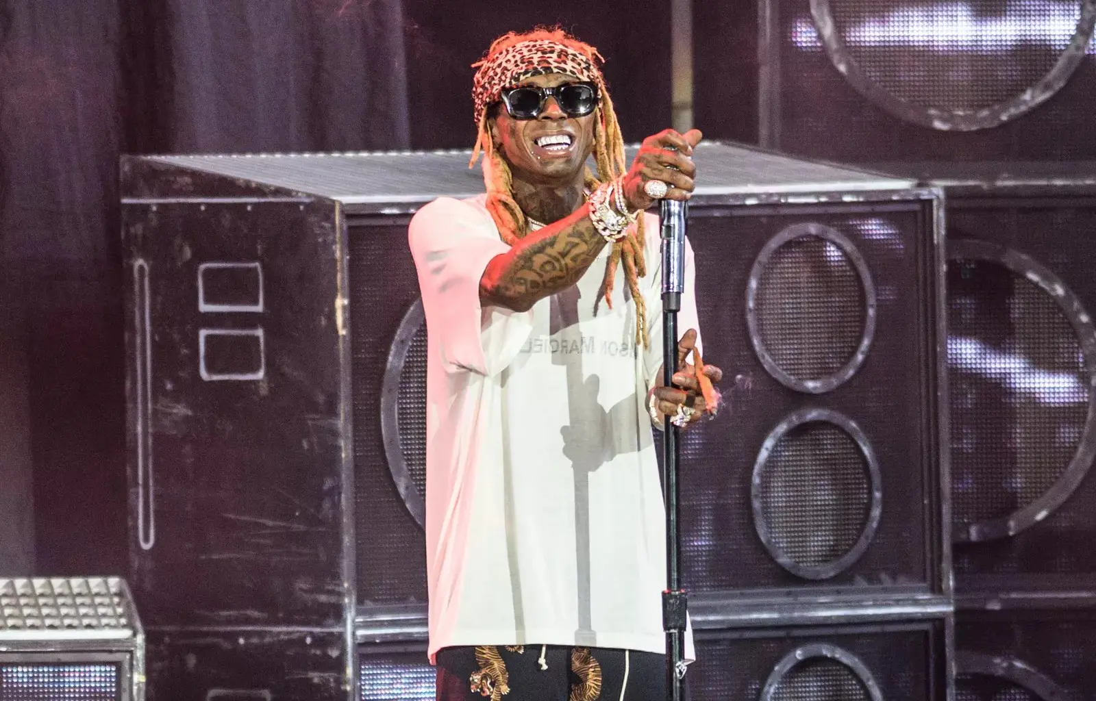 lil wayne stands on stage at house of blues wearing sunglasses and a white shirt while holding a mic toward the crowd