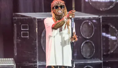 lil wayne stands on stage at house of blues wearing sunglasses and a white shirt while holding a mic toward the crowd