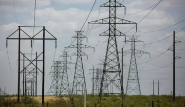 Several towers carrying electrical transmission lines crowd a swath of rural land.