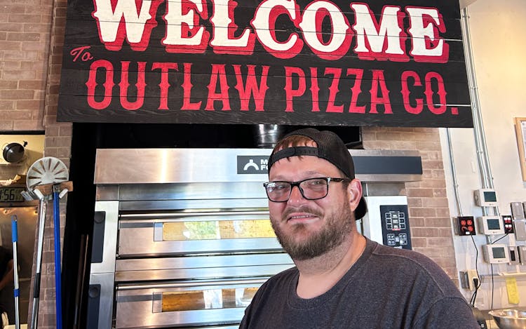 photo of pitmaster in front of outlaw pizza sign