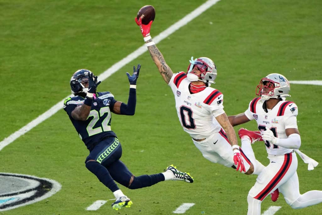 Could Dallas Pull Off A Deion Sanders-Level Move? Christian Gonzalez leaps with one hand extended toward the football during a New England Patriots game against the Seattle Seahawks.
