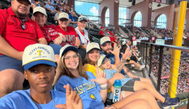 A group of fans at a baseball game wearing matching caps.