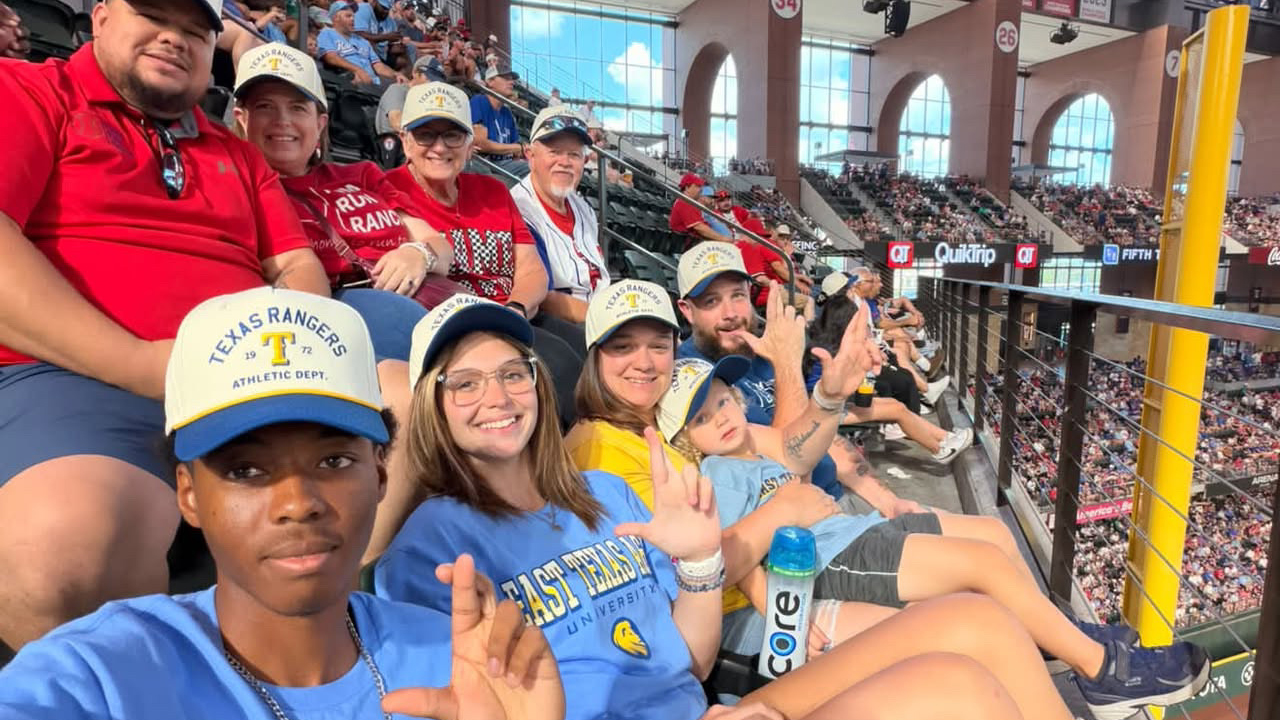 A group of fans at a baseball game wearing matching caps.