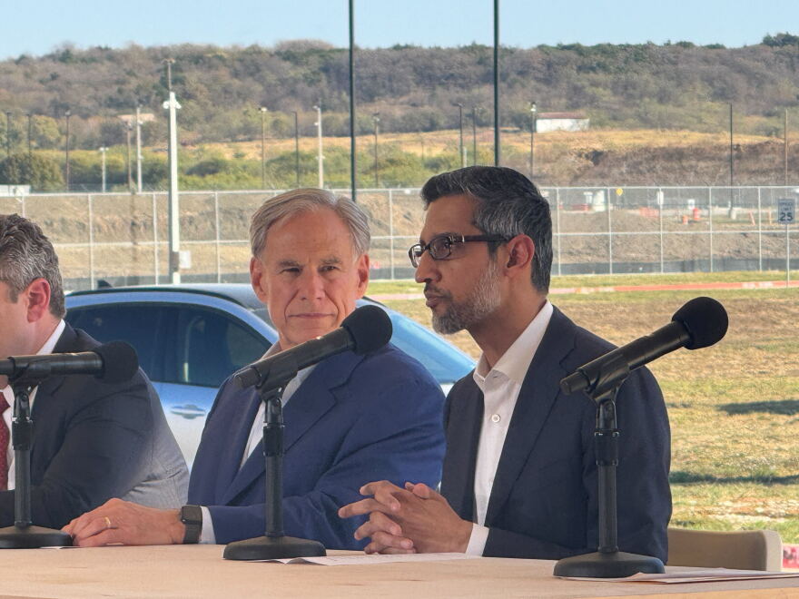 Two men sitting next to each other and speaking into microphones.