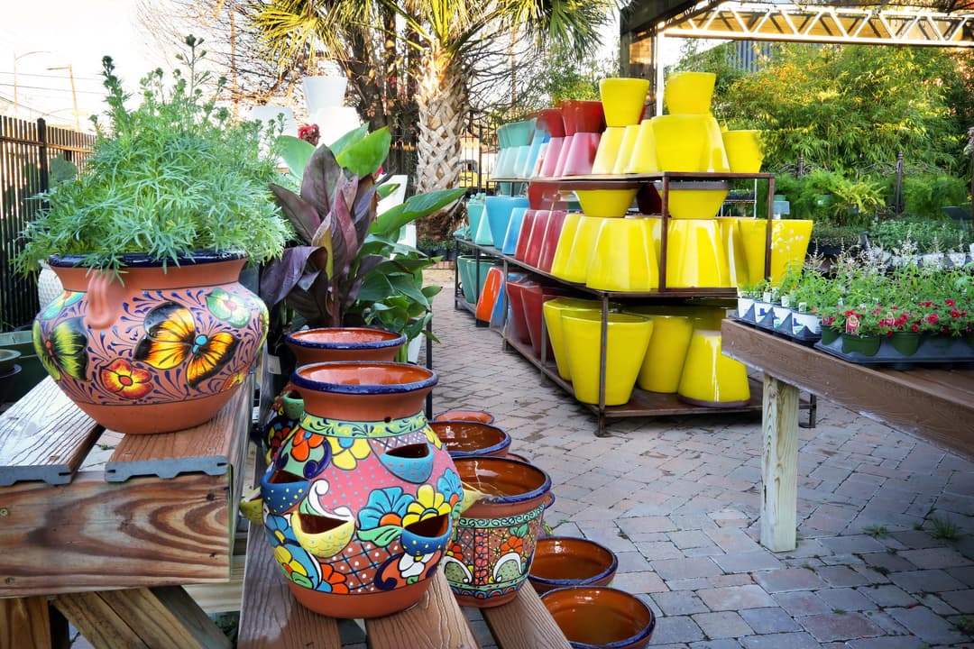 Outdoor garden center display with colorful Talavera pottery, yellow ceramic pots, and potted plants on brick pavers.
