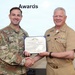 NAMRU San Antonio Director awarded Navy and Marine Corps Commendation Medal for Meritorious Service Two military officers are shaking hands while jointly holding an award certificate during a formal awards ceremony. The certificate is from the Department of the Navy and appears to be a Navy and Marine Corps Commendation Medal. One officer is in U.S. Army combat uniform and the other is in U.S. Navy service khaki uniform.