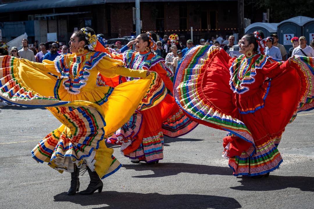 Women dance in the street with long colorful dresses during a previous Viva la Vida Festival & Parade. 