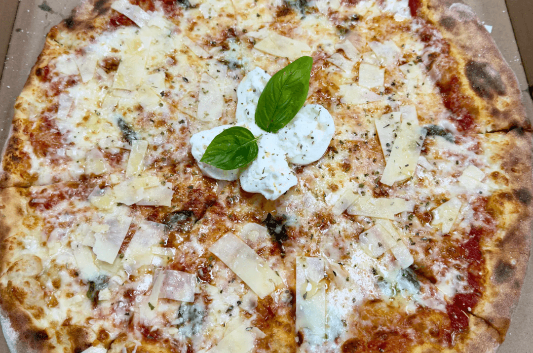 Pizza topped with fresh mozzarella, basil leaves, shaved parmesan, and herbs in a cardboard box.
