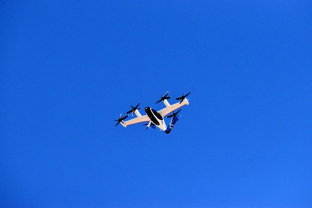 White electric air taxi with multiple rotors flying against a clear blue sky.