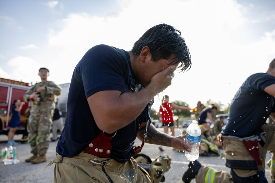 A kneeling man in a firefighter uniform splashes water on his face from a bottle.